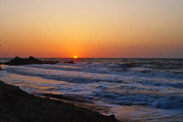 Sunrise on the seashore with waves on a warm summer morning