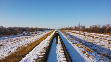Fototapeta premium Solitary Figure Walking Down the Center of a Long, Straight Railway Track in Winter