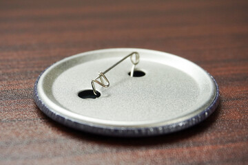Backside of metal round safety pin isolated on horizontal brown wooden table surface background.