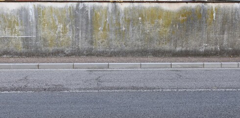 Grunge plaster wall peeled stained with mold and lichens. Sidewalk  and street in front. Background for copy space.