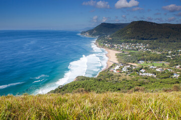 The iconic view looking south to Stanwell Park beach and the famous Sea Cliff Bridge from the Illawarra's Bald Hill Lookout. Captured on a blue sky sunny day from the grassy knoll.
