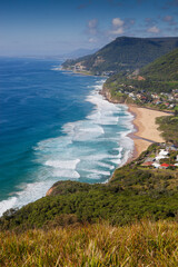 The iconic view looking south to Stanwell Park beach and the famous Sea Cliff Bridge from Bald Hill Lookout. Captured on a blue sky sunny day from the grassy knoll.