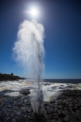 The famous Little Blowhole situated in the beautiful coastal town of Kiama in New South Wales Australia, spouting water high into the air with natural ocean force. Captured on a blue sky sunny day.