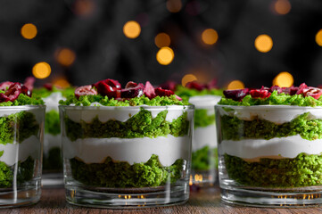 Small green desserts for a party, sponge cake with spinach, layered with whipped cream, decorated with freeze-dried fruit