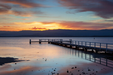 Boonerah Point jetty under a beautifully vibrant sky looking west to the mountains on Lake Illawarra, NSW, Australia.