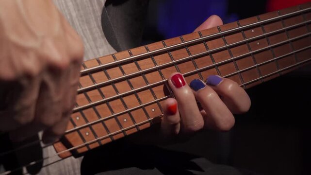 Close up of finger musician at the bass guitar , musician playing bass guitar in the room and with  spotlights ,Bassist practicing in a  studio.