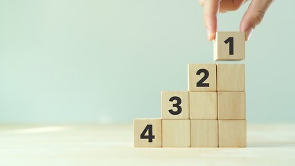 A hand places a wooden block with the number one on top of a stack of blocks numbered two, three, and four, symbolizing growth and progress.