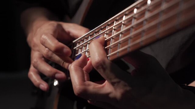 Close up of finger tapping bass of musician at the bass guitar , musician playing bass guitar in the room and with spotlights ,Bassist practicing in a  studio.