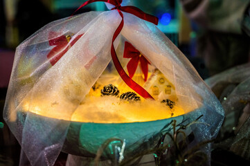 Glowing decorative light arrangement wrapped in sheer fabric with red ribbon, pine cones, cozy festive atmosphere, magical illumination, holiday decor concept, warm mood, creative still life