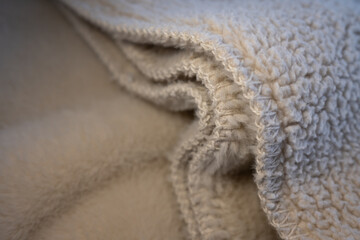 Macro detail of soft, folded sherpa fleece fabric. The warm beige texture and stitching create a cozy, abstract background for comfort and winter concepts. ©  Colorshadow