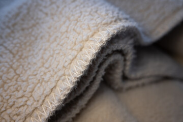 Macro shot of a soft, warm, cream-colored sherpa fleece fabric. The focus is on the textured material and stitched edge, creating a cozy and comfortable background. ©  Colorshadow