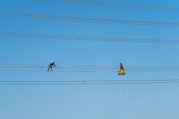 Aerial view of linesmen navigating the high-tension wires against the vivid blue canvas of the sky, Joypurhat, Rajshahi Division, Bangladesh.