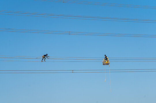 Aerial view of linesmen navigating the high-tension wires against the vivid blue canvas of the sky, Joypurhat, Rajshahi Division, Bangladesh.