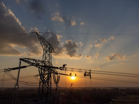 Aerial view of silhouettes of workers atop a towering transmission tower against a vibrant sunset, Joypurhat, Rajshahi Division, Bangladesh.