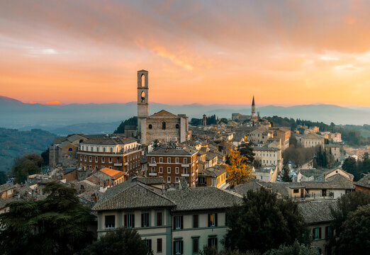Aerial view of terracotta rooftops cascade down the hillside, anchored by the stoic presence of the Church of Sant'Agostino under a pastel sky, Morcella, Umbria, Italy.