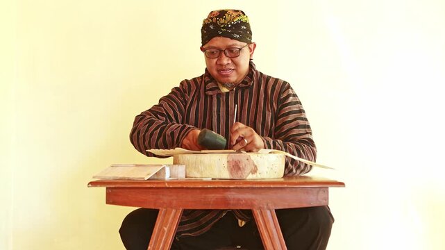 Javanese craftsman carving wood with a chisel and hammer