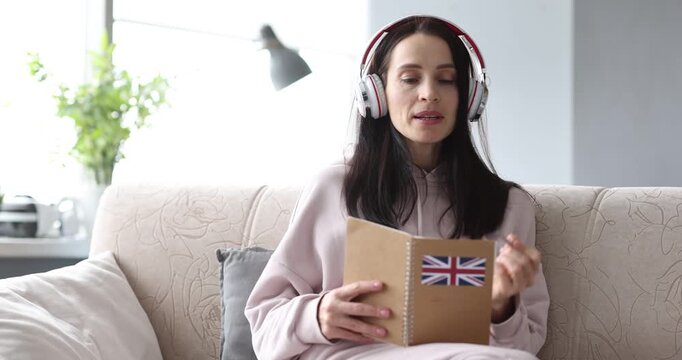 Woman in headphones sits on sofa reading book with British flag on cover. Learner practices English pronunciation repeating new words from page