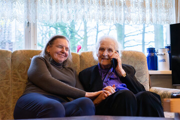 Elderly woman talking on phone with daughter supporting her