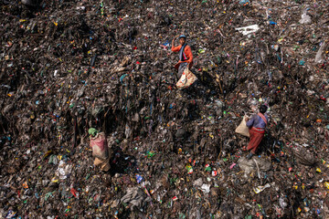 Aerial view of figures in vibrant clothing amidst a sprawling landfill, a stark contrast of human presence against a dark, textured landscape, Dhaka, Dhaka Division, Bangladesh.