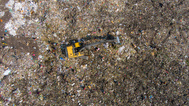 Aerial view of a yellow excavator amidst a vast, textured landscape of waste, contrasting industrial machinery with environmental concern, Dhaka, Dhaka Division, Bangladesh.
