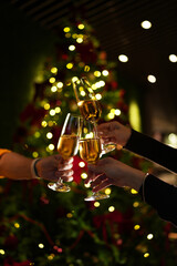 Hands raising glasses of champagne for a festive toast in front of a decorated Christmas tree. Warm holiday atmosphere, bokeh lights, celebration mood and New Year party vibes.