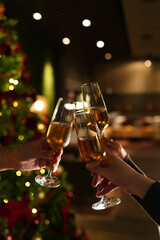 Naklejka premium Hands raising glasses of champagne for a festive toast in front of a decorated Christmas tree. Warm holiday atmosphere, bokeh lights, celebration mood and New Year party vibes.