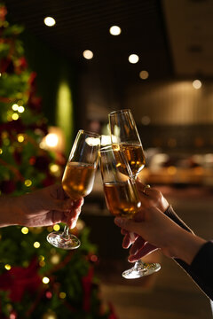 Hands raising glasses of champagne for a festive toast in front of a decorated Christmas tree. Warm holiday atmosphere, bokeh lights, celebration mood and New Year party vibes.