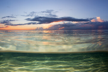 An under over split view of an idyllic clear water sandy beach captured on sunrise. 