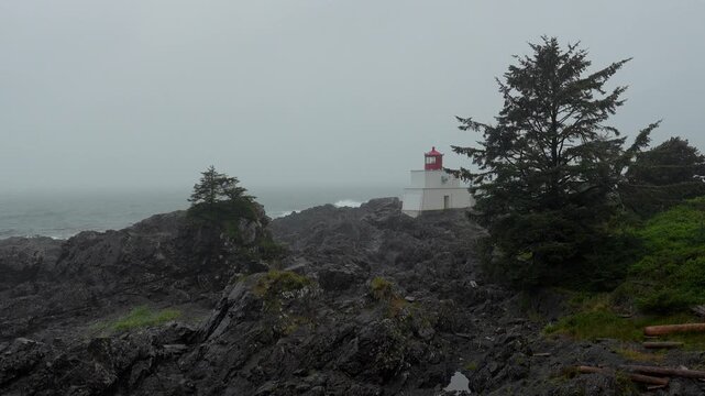 Fog obscures the amphitrite point lighthouse, a picturesque landmark nestled amidst rugged rocks and coniferous trees on the coast of ucluelet, vancouver island, british columbia, canada