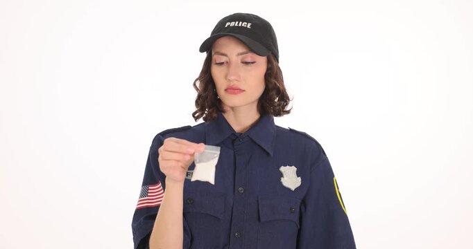 Woman police officer in dark uniform inspects small plastic evidence bag. Serious law enforcer studies suspicious powder preparing crime report