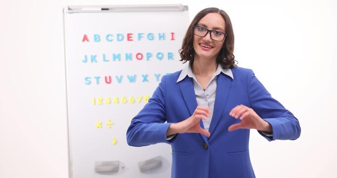 Woman teacher in blue blazer stands near board with colorful alphabet. Smiling educator teaches basic English letters enjoying friendly school lesson