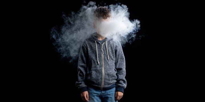 Teen male vaping smoke obscuring face on dark background