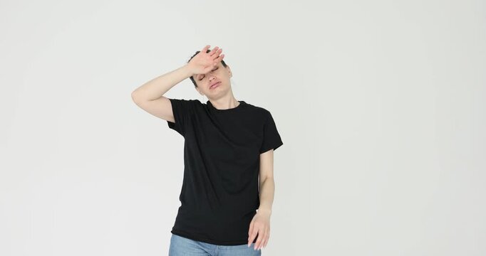 Woman in black T-shirt wipes sweat from forehead against white background. Female with hair gathered into neat bun lets out heavy sigh. Slow motion