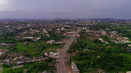 Aerial view of a sprawling cityscape meeting lush greenery, divided by a stark, grey road slicing through the landscape, Akure, Ondo, Nigeria.