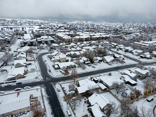 Aerial view of a snow-blanketed suburban neighborhood with houses and streets under a veil of winter's quietude, Layton, Utah, United States.