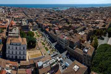 Obraz premium Aerial view of a square with gardens in the historic center of Catania, Sicily, southern Italy. In the background, the city port and the Mediterranean Sea on the horizon It's a sunny summer morning.