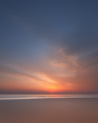 a serene beach at sunset, with the sky painted in hues of orange and blue
