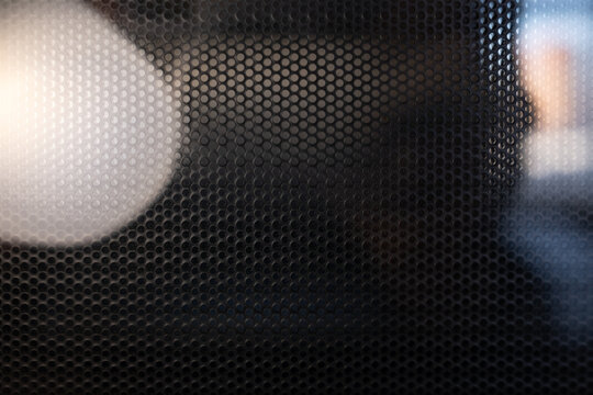 Macro shot of a black perforated industrial grille. The textured surface creates a geometric pattern with blurred lights and reflections for an abstract effect. - Powered by Adobe