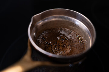 Close-up of traditional Turkish coffee brewing in a cezve. The dark, rich foam bubbles up on a black stove, invoking a morning ritual.
