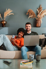 Joyful couple sharing moments together as they use their smartphone and laptop, capturing the...