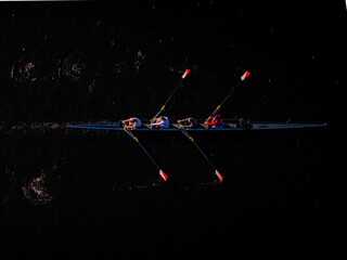 Aerial view of rowers slice through the dark waters of the Charles River, each stroke a flash of red and white against the inky black, Boston, Massachusetts, United States.