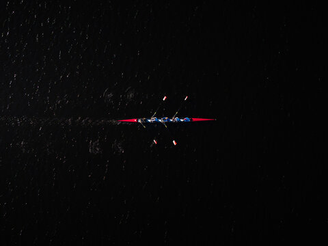 Aerial view of a rowing team slicing through the dark waters of the Charles River, their oars creating fleeting ripples, Boston, Massachusetts, United States.