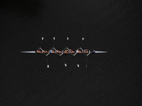 Aerial view of a rowing team gliding across the Charles River's dark waters, their oars creating subtle ripples, Boston, Massachusetts, United States.