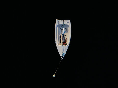 Aerial view of a small white sailboat cuts through the dark expanse of water, its angular form a stark contrast against the inky depths, Boston, Massachusetts, United States.