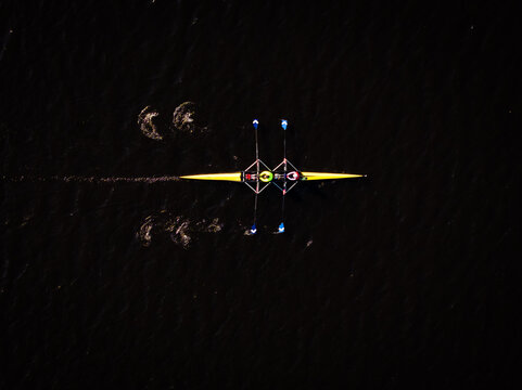 Aerial view of a yellow rowing boat cutting through the dark, rippled waters, a stark contrast under the open sky, Boston, Massachusetts, United States.