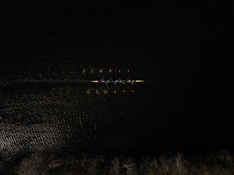 Aerial view of rowing team cutting through the dark waters of the Charles River, the oars reflecting the dim lights, Boston, Massachusetts, United States.