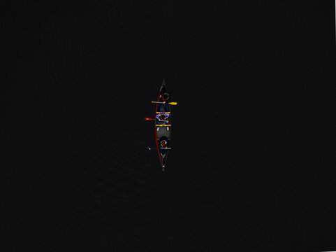 Aerial view of a solitary canoe slicing through the dark waters, a tiny vessel carrying figures in the vast expanse, Boston, Massachusetts, United States.