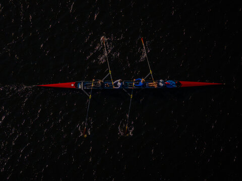 Aerial view of a sleek, red-tipped rowing shell slicing through the inky waters, leaving delicate wakes in its path, Boston, Massachusetts, United States.
