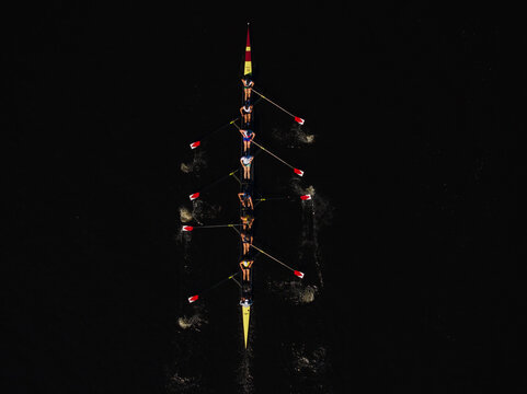 Aerial view of a rowing team slicing through the dark waters, their oars creating rhythmic patterns, a testament to teamwork and precision, Boston, Massachusetts, United States.