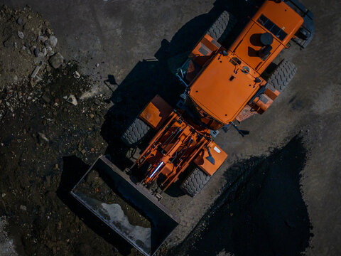 Aerial view of an orange bulldozer casts a stark shadow on the rough, gray terrain, a symphony of industrial grit, Boston, Massachusetts, United States.